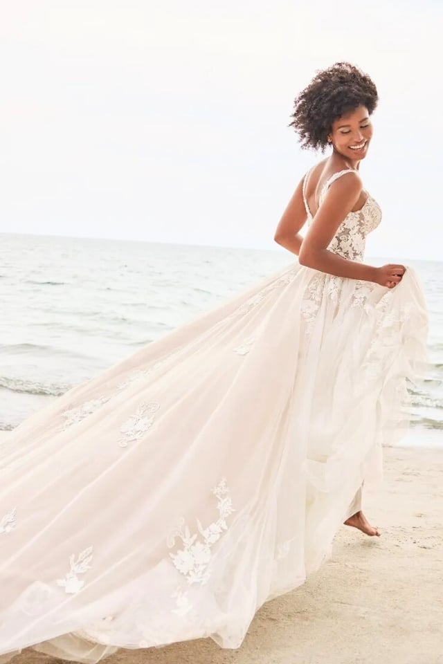 Beachy Lace A-Line Wedding Dress Palmer MT3240 Bride on beach wearing sleeveless A-line wedding gown with lace appliqués, deep V-neckline, and long flowing train.