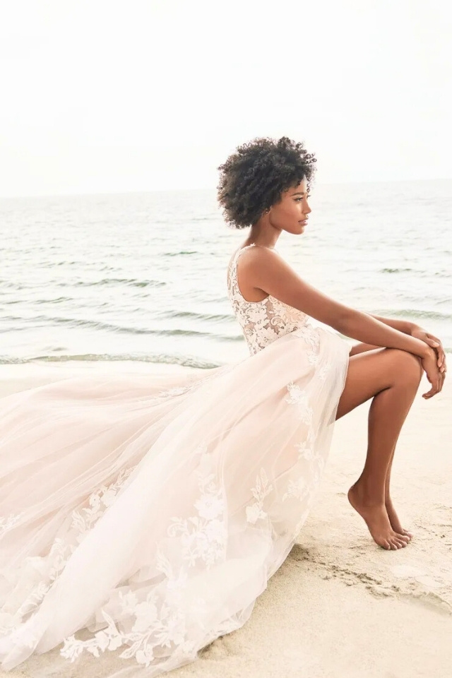 Beachy Lace A-Line Wedding Dress Palmer MT3240 Bride on beach wearing sleeveless A-line wedding gown with lace appliqués, deep V-neckline, and long flowing train.