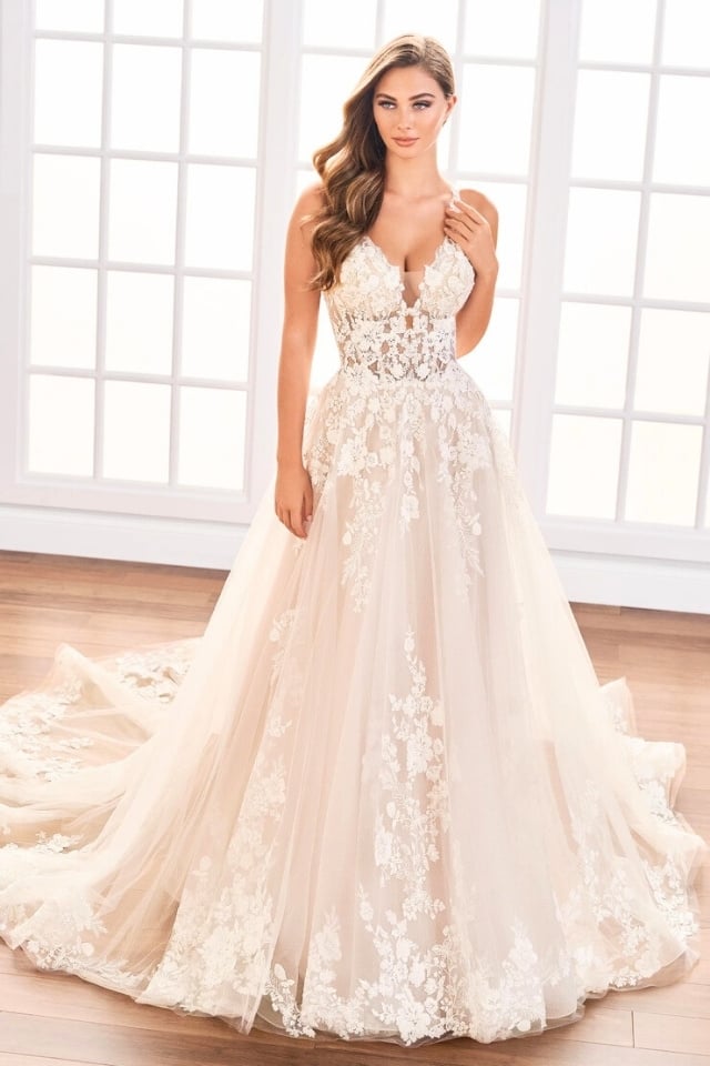 Bride wearing a floral lace and sparkle tulle A-line gown with sweetheart neckline, posing in front of large windows with natural light.