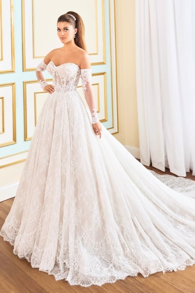 Bride wearing a romantic lace A-line wedding gown with sweetheart neckline and long lace train, styled with detachable long sleeves.