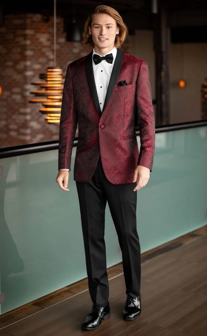 Bold apple red paisley Aries tuxedo by Mark of Distinction featuring a statement-patterned jacket, black satin lapels, tailored black trousers, crisp white dress shirt, and black bow tie for a standout formal look
