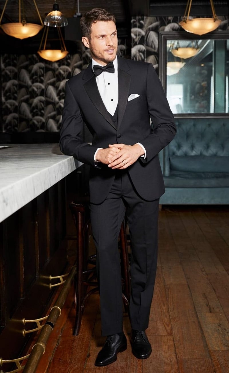 Michael Kors Black Legacy Performance tuxedo featuring a tailored black jacket with satin lapels, matching trousers, white dress shirt, black bow tie, and polished black oxford shoes, styled for formal occasions