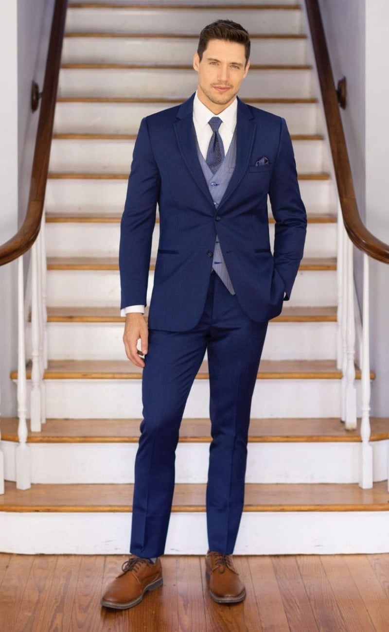 Michael Kors blue performance wedding suit featuring a tailored blue jacket and trousers, coordinating vest, white dress shirt, blue tie, and brown oxford shoes, styled for a modern formal wedding look