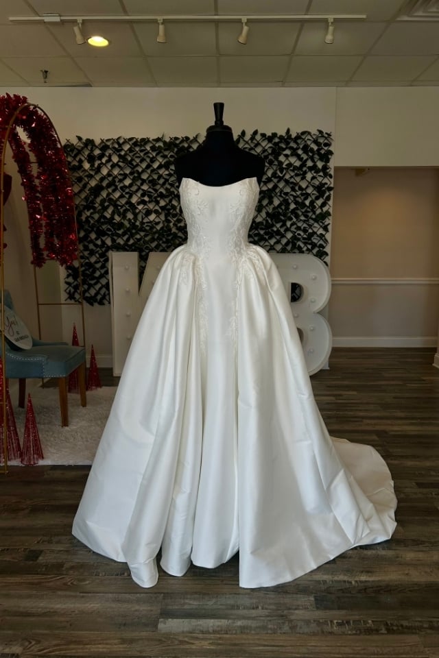 Page Updates & Announcements Strapless satin ball gown wedding dress with lace bodice details displayed on mannequin in bridal boutique.