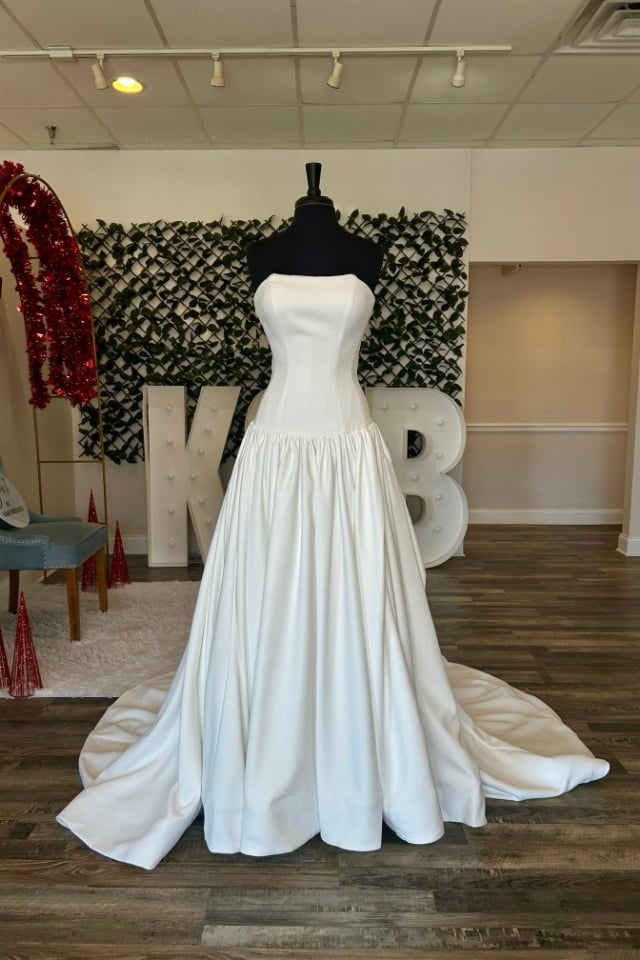 Page Updates & Announcements Strapless satin drop-waist wedding dress with full gathered skirt displayed on mannequin in bridal boutique.