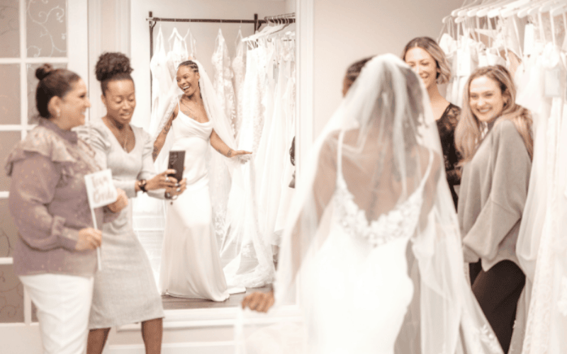 bride happily smiling in front of the mirror while friends are taking pictures and smiling