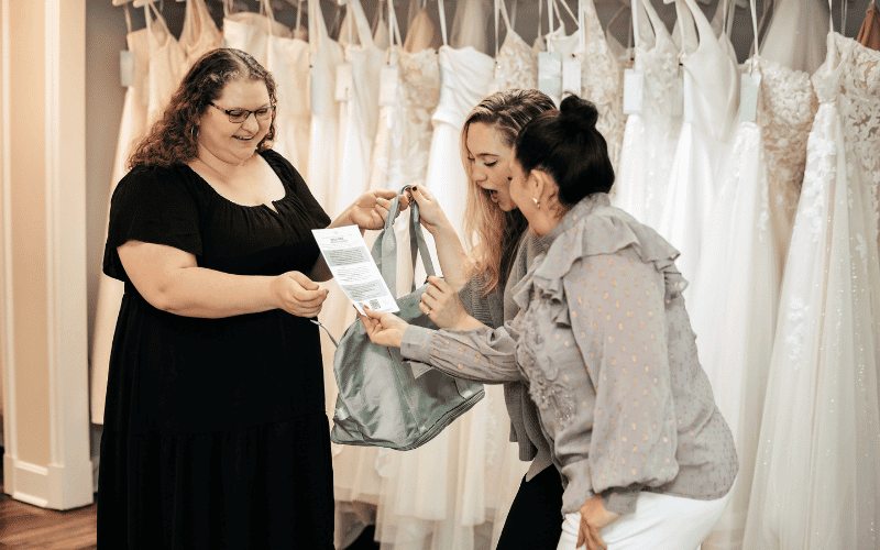 How to Find the Perfect Wedding Dress Beyond Your Pinterest Board three woman laughing looking at a paper