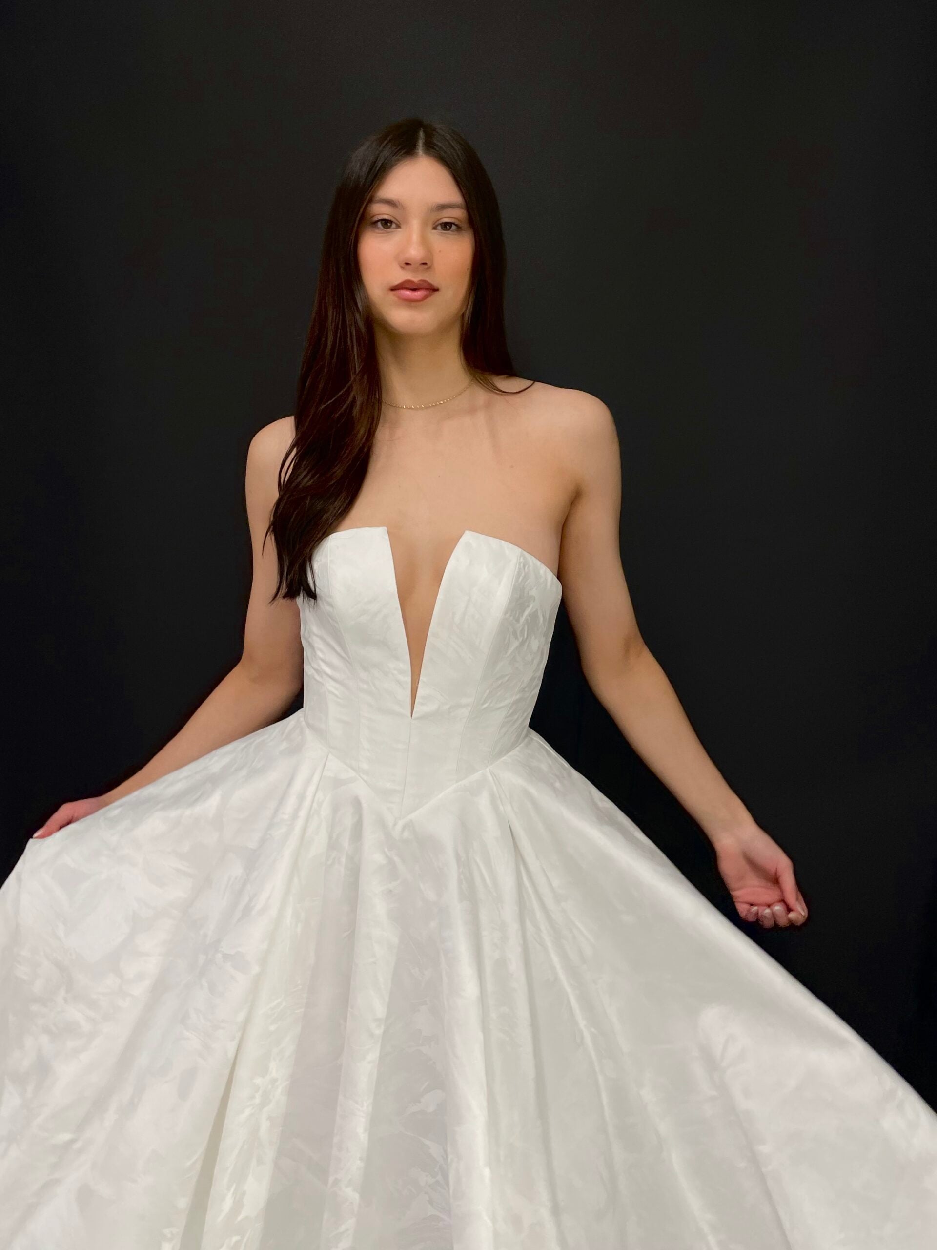 Allison strapless floral jacquard ball gown wedding dress featuring a dramatic plunging V-neckline, structured fitted bodice, pointed basque waistline, and voluminous pleated skirt with subtle botanical detailing.