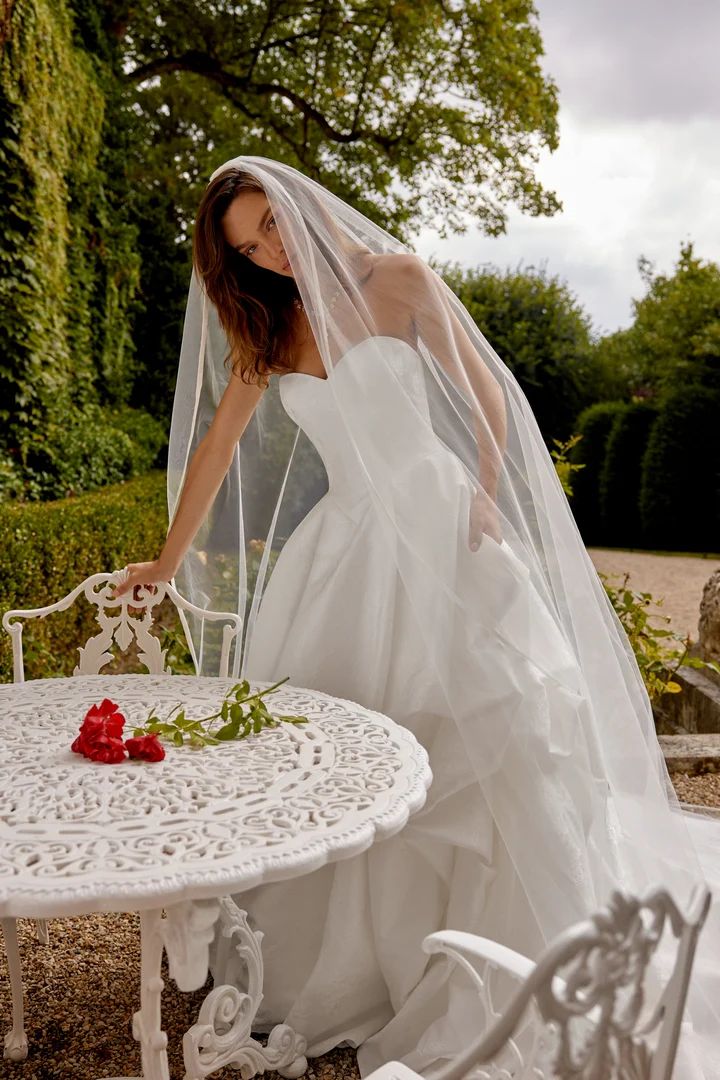 Mara by Justin Alexander strapless brocade ball gown wedding dress featuring a sweetheart neckline, structured bodice, basque waistline, voluminous skirt, covered back buttons, and chapel-length train.