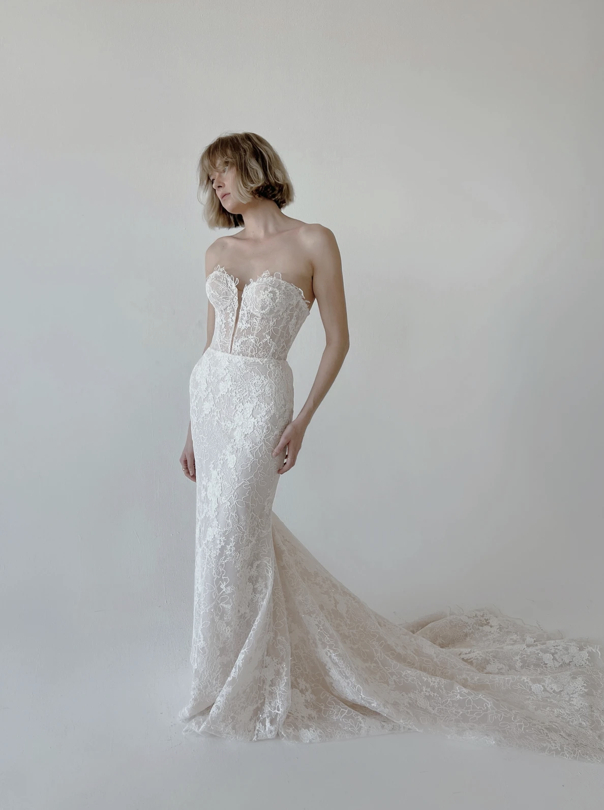 Huntington strapless embroidered fit and flare wedding dress featuring a narrow plunging V-neckline, sheer corset bodice, intricate floral lace detailing, lace-up corset back, and sweeping lace train.