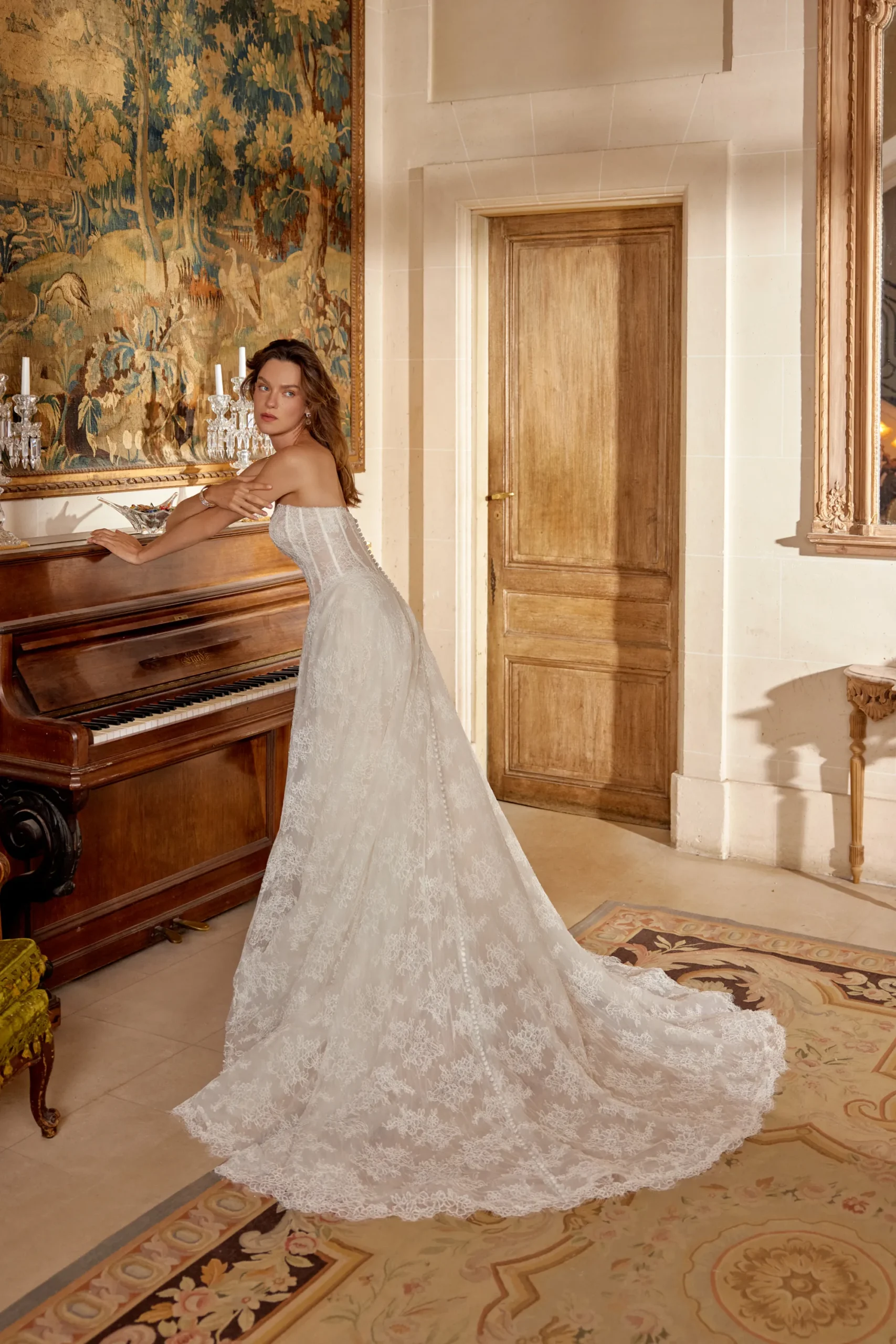 Strapless Lace A-Line Wedding Dress Manuela Manuela by Justin Alexander ivory lace A-line wedding dress featuring a strapless straight neckline, structured corset bodice, basque waistline, flowing lace skirt, side pockets, and chapel-length train.